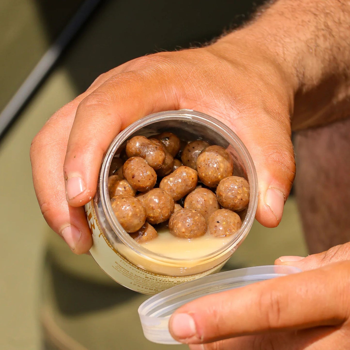 OMC iScream Nutty Sauce Infused Hookbaits open tub in angler's hands showing mixed hookbaits and sauce